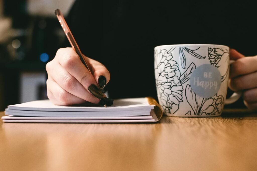 A person writing while holding a cup