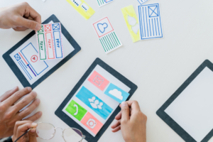 Two people arranging web design layouts with cut papers on a table