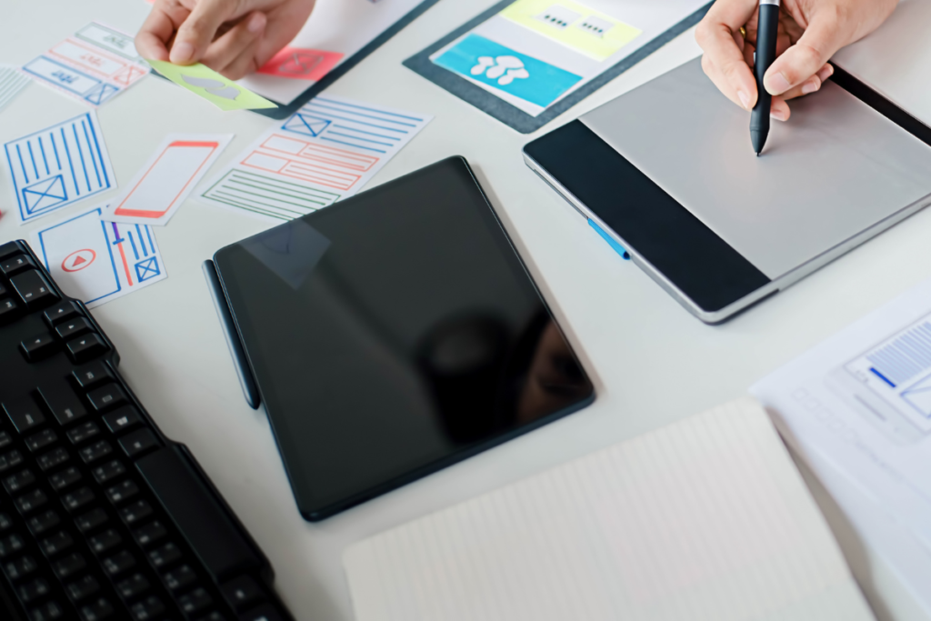 Web designers working on a tablet layout with cut paper designs on a table