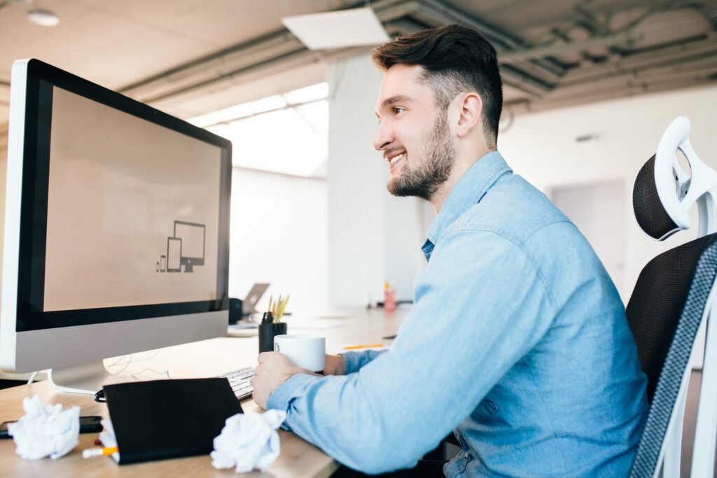 Young man in blue shirt is sitting at his workplace in office