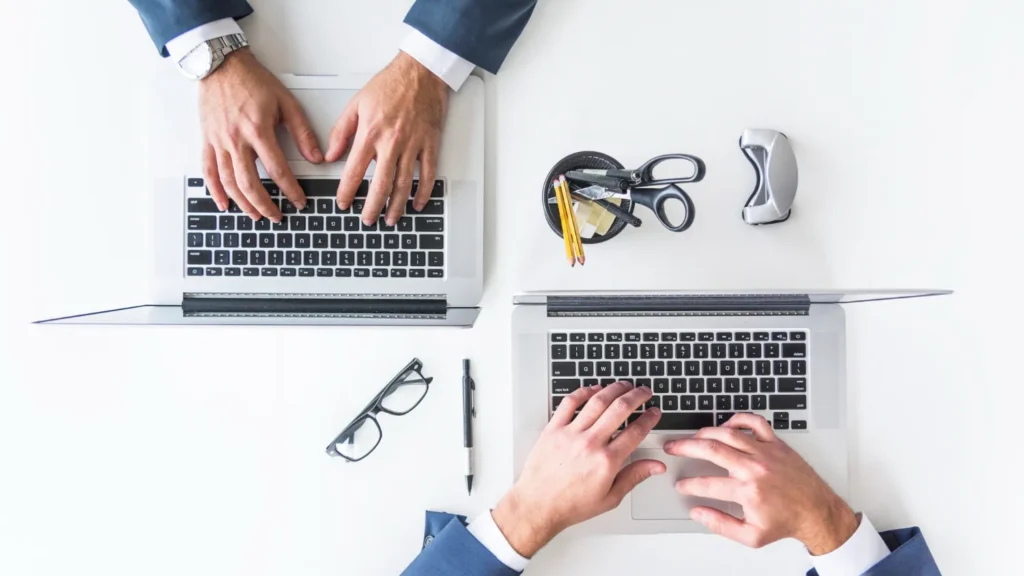 An overhead view of a businessman's hand typing on a laptop over a white table
